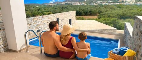 A couple and a child by a pool with a view of a mountainous landscape.