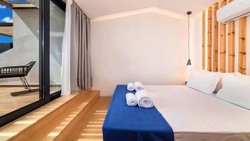A modern hotel room with a bed, a blue towel, a wooden headboard, and a glass door leading to an outdoor area.