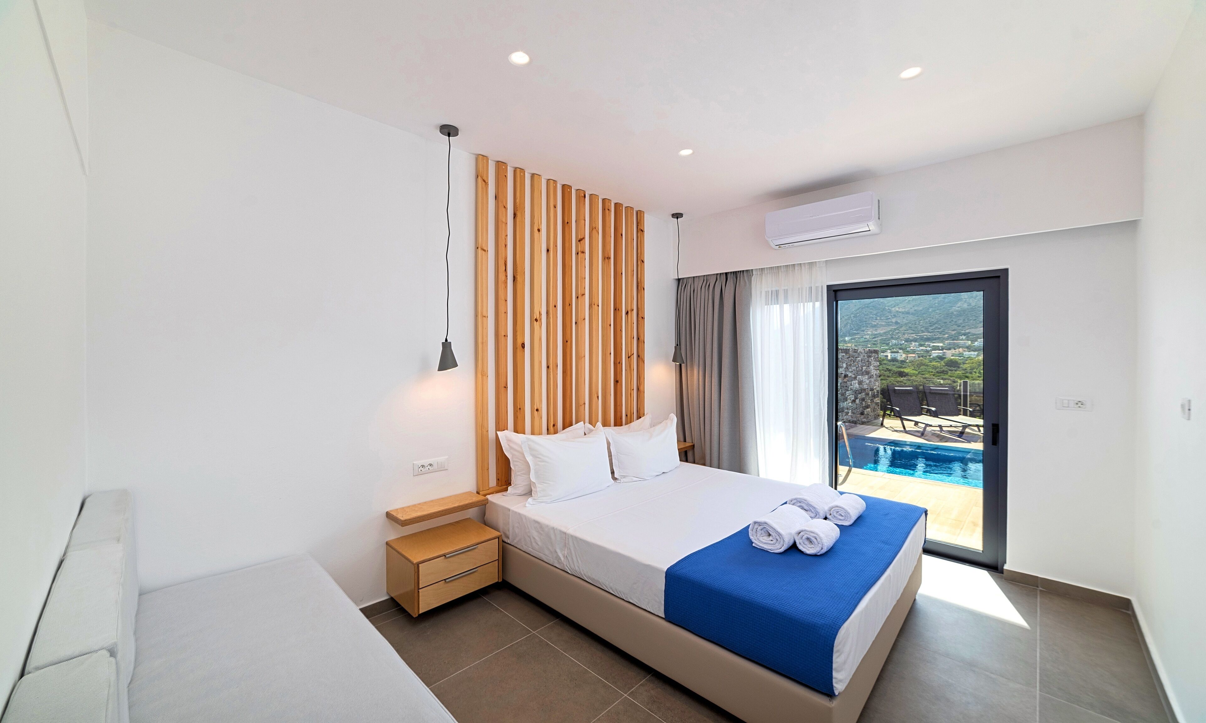 A modern hotel room with a large bed, a wooden accent wall, a view of a pool, and a balcony.