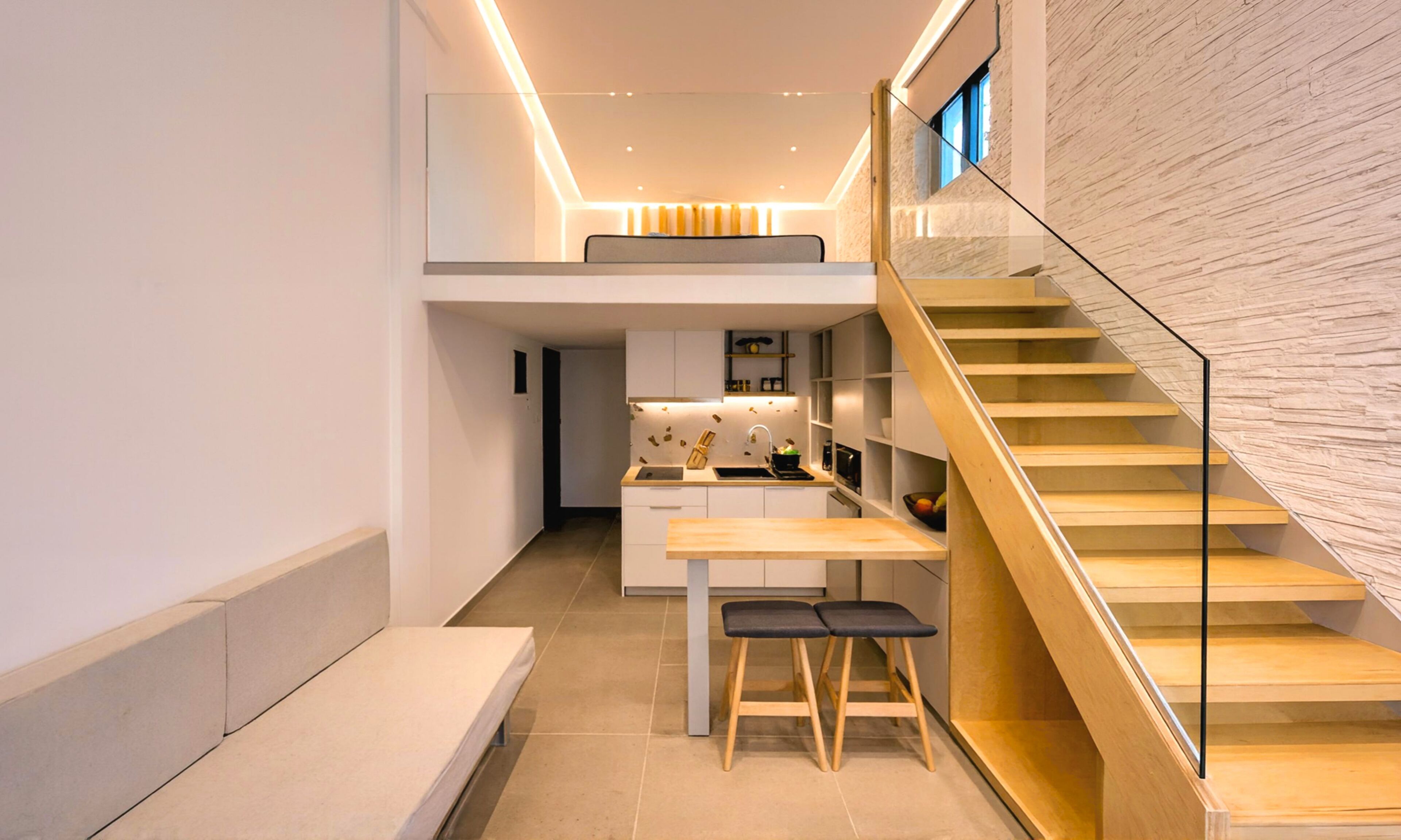 A modern kitchen with a central island, a dining area with stools, and a staircase leading to an upper level.