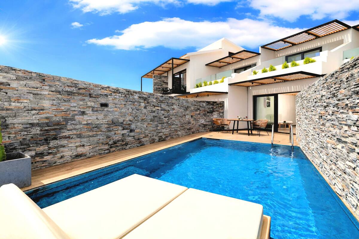 A modern house with a swimming pool, stone walls, and outdoor furniture.