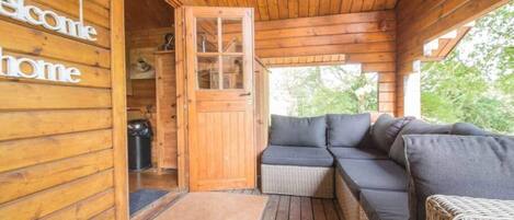 A wooden cabin with a welcoming sign, a glass door, a wicker sofa, and a wicker chair.