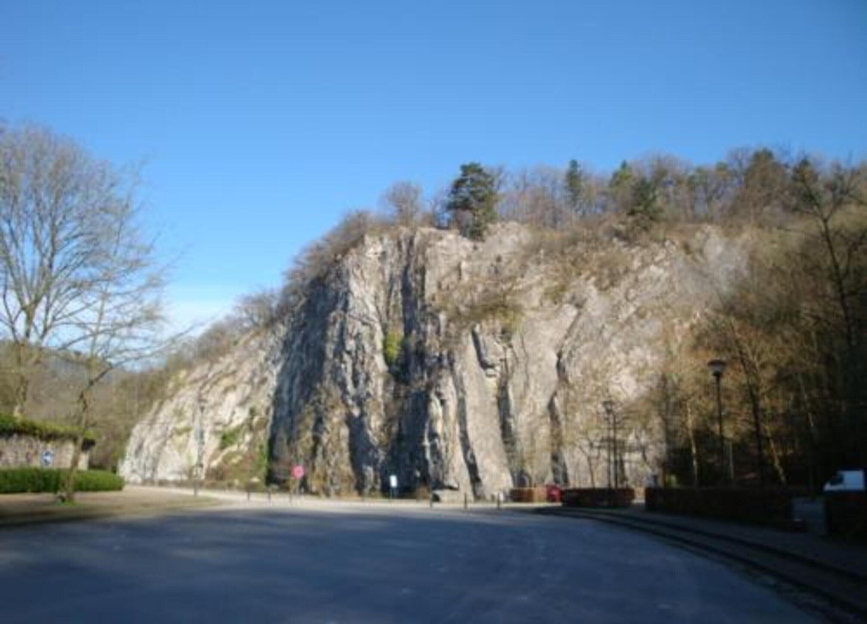 A road leading to a rocky cliff with sparse trees and a clear sky.