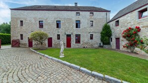 Un bâtiment en pierre doté d’une cour, d’une statue et d’une plante à fleurs rouges.