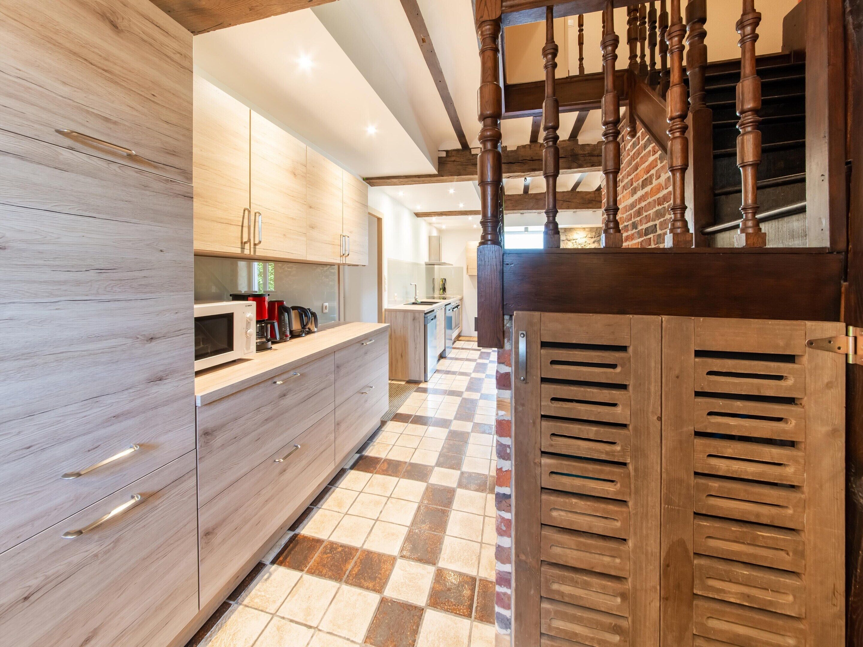 A modern kitchen with wooden cabinets, a checkered floor, and a staircase with wooden balusters.