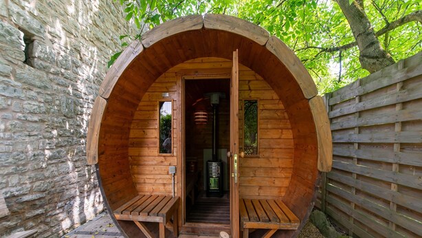 Une structure circulaire en bois, dotée d’une porte et de deux bancs à l’intérieur.