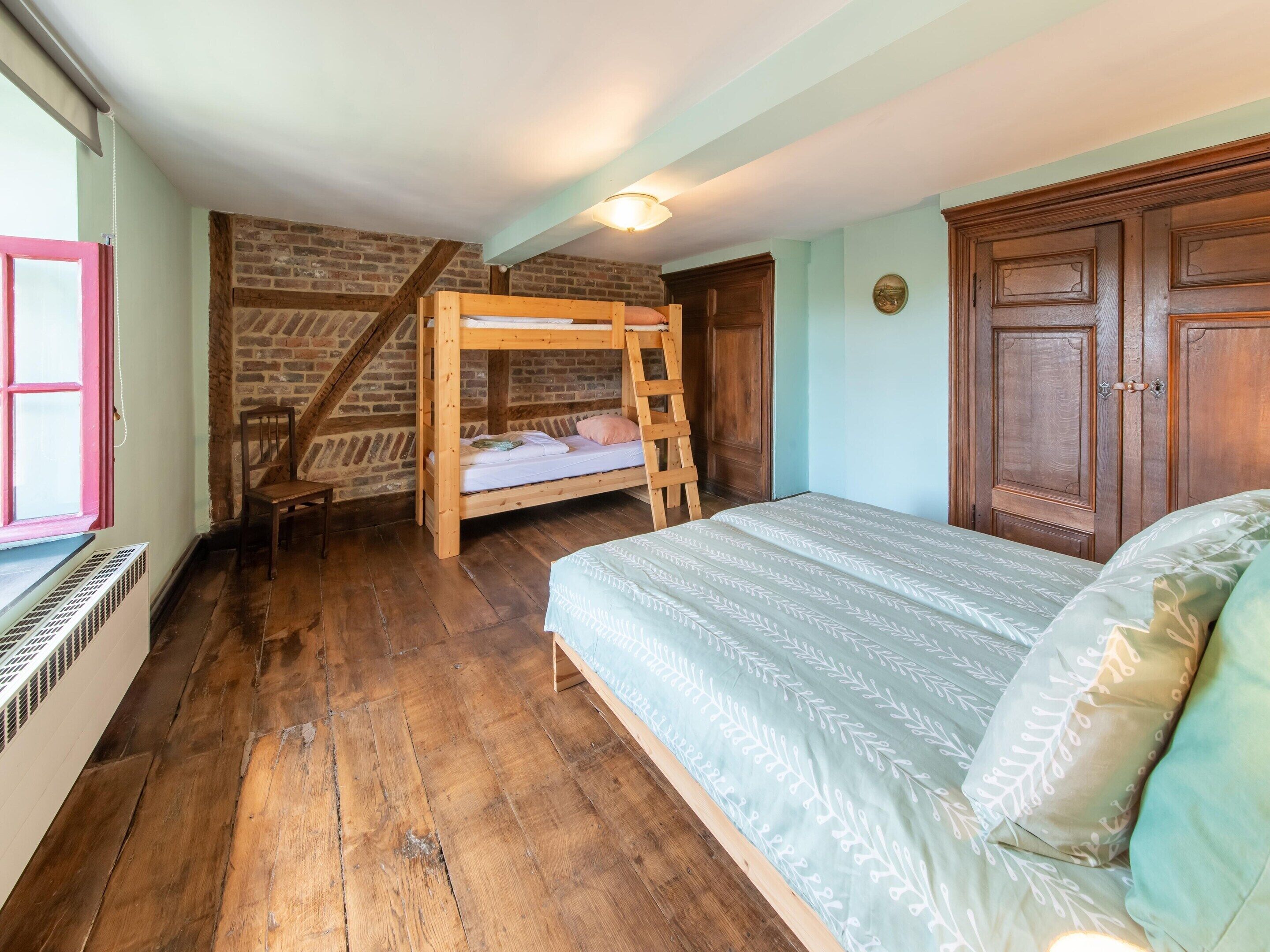 Ein Zimmer mit Etagenbett, Holzboden, Backsteinwand und großem Holzschrank.