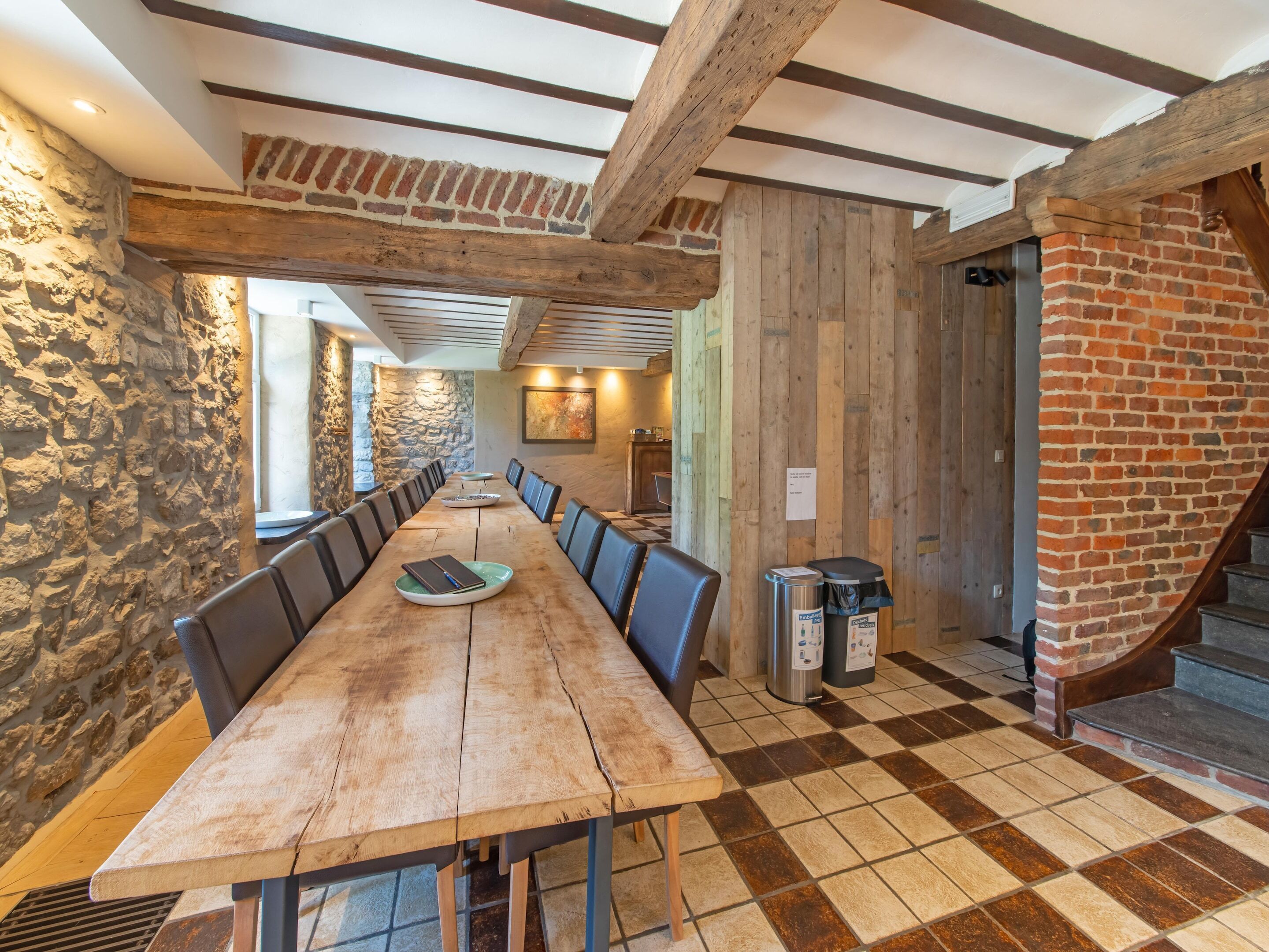 Ein langer Holztisch mit Stühlen, eine Steinwand und eine Treppe.