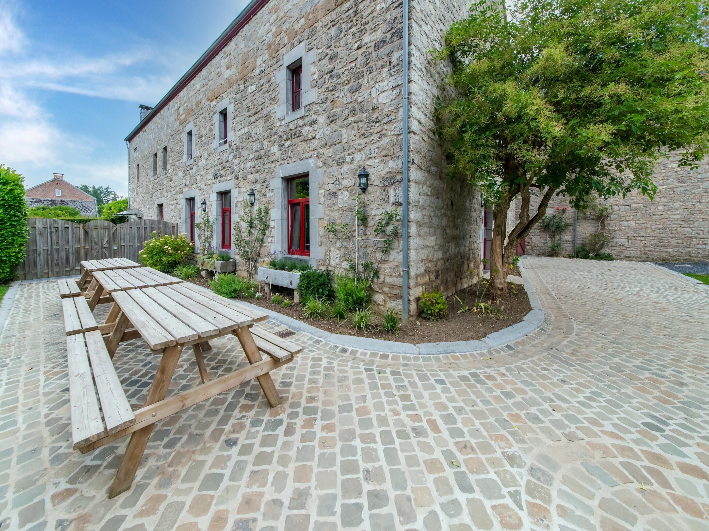 Un bâtiment en pierre doté d’une cour, de tables de pique-nique et d’un arbre.