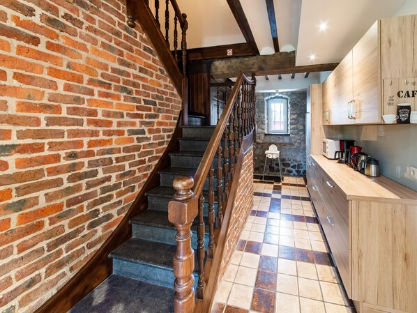 Una cocina con escalera de madera, pared de piedra y piso de baldosas.