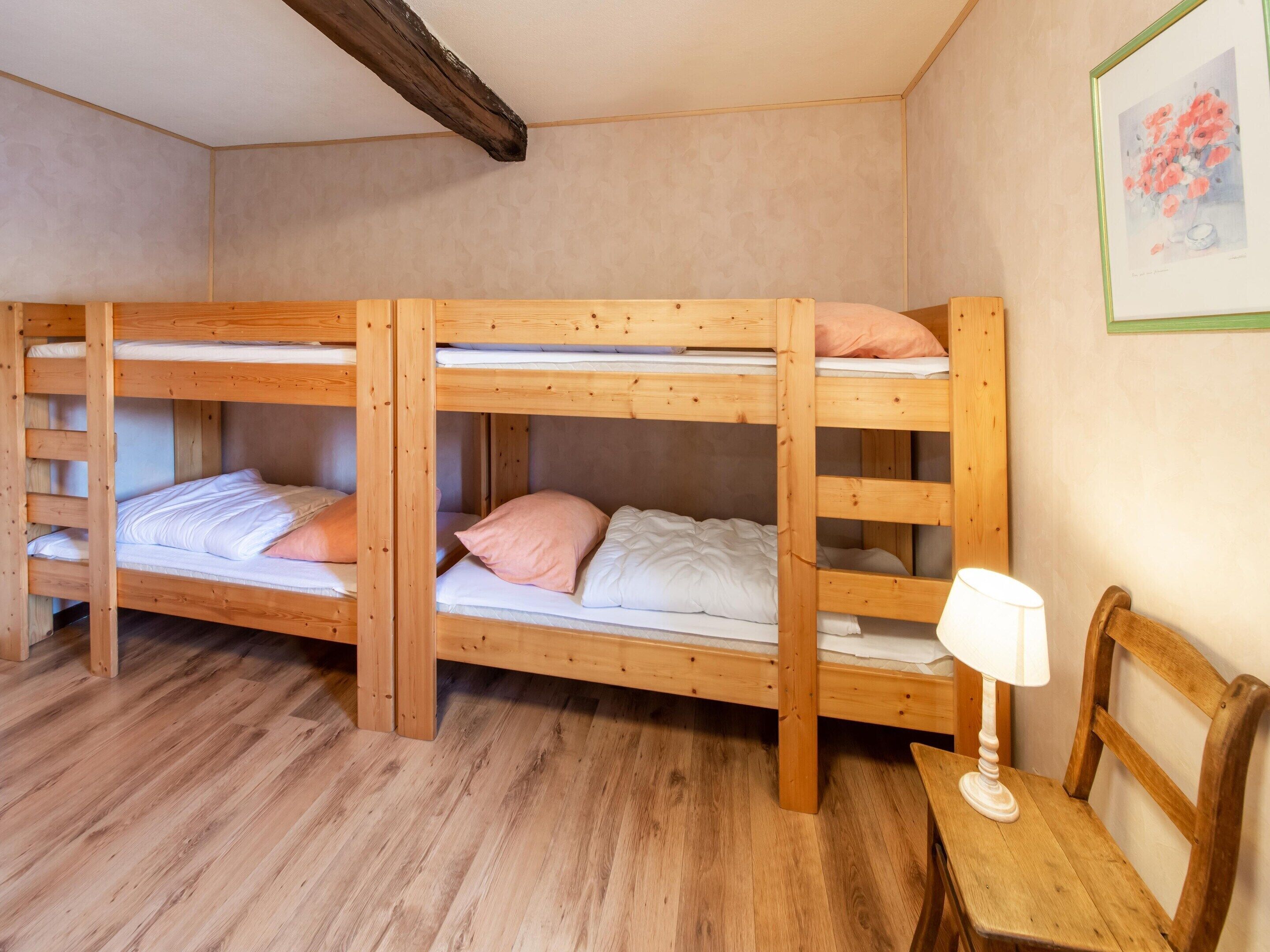Una habitación con tres literas, una mesa de madera con una lámpara y un cuadro en la pared.