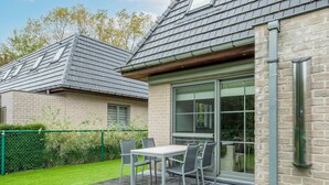 Une maison moderne dotée d’un patio, d’une table et de chaises, ainsi que d’une pelouse verdoyante.