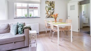 Un salon moderne avec un canapé, une table à manger et des chaises, un radiateur, une fenêtre avec des plantes et un tableau accroché au mur.