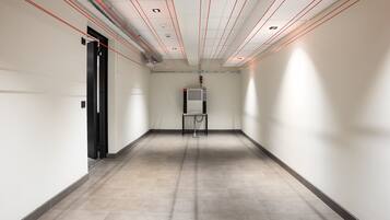 A hallway with a tiled floor, a black door on the left, and a wall-mounted air conditioning unit in the center.