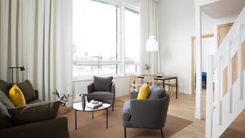 A modern living room with a sofa, armchair, and coffee table, a dining area with a table and chairs, and a staircase leading to another level.