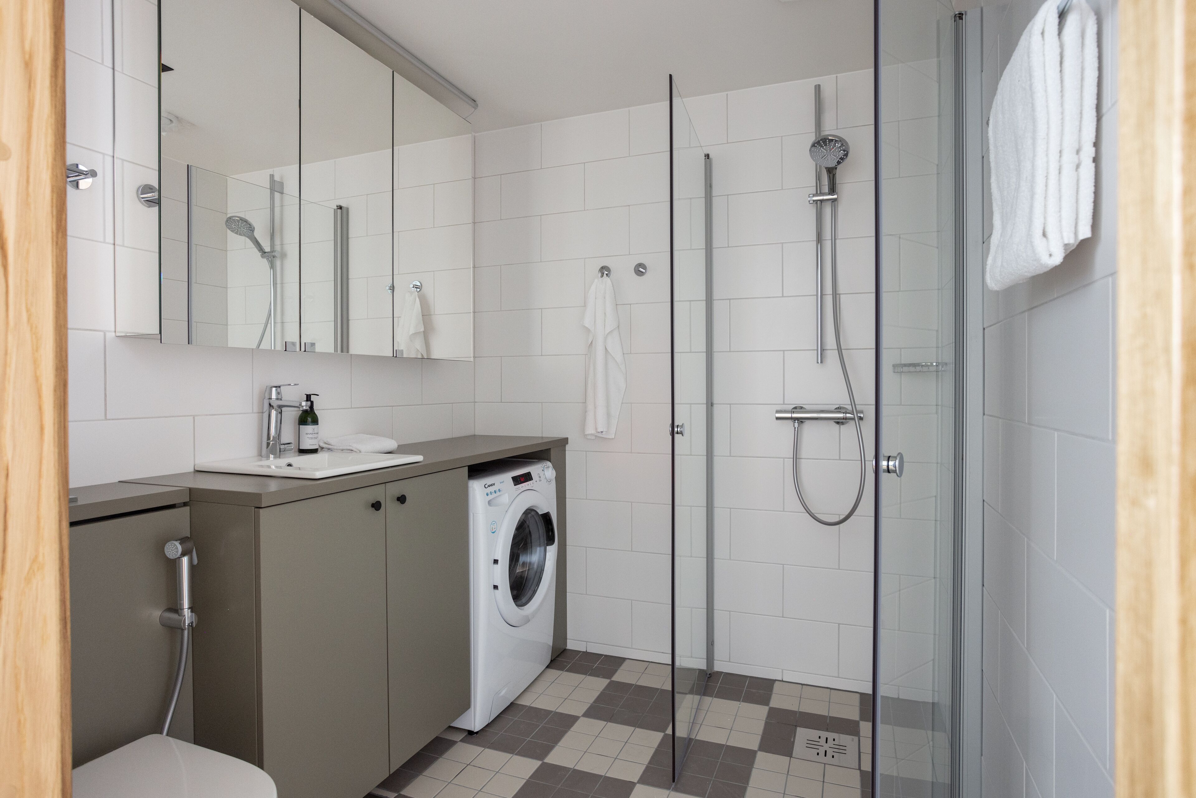 A modern bathroom with a glass shower enclosure, a built-in washing machine, and a large mirror.