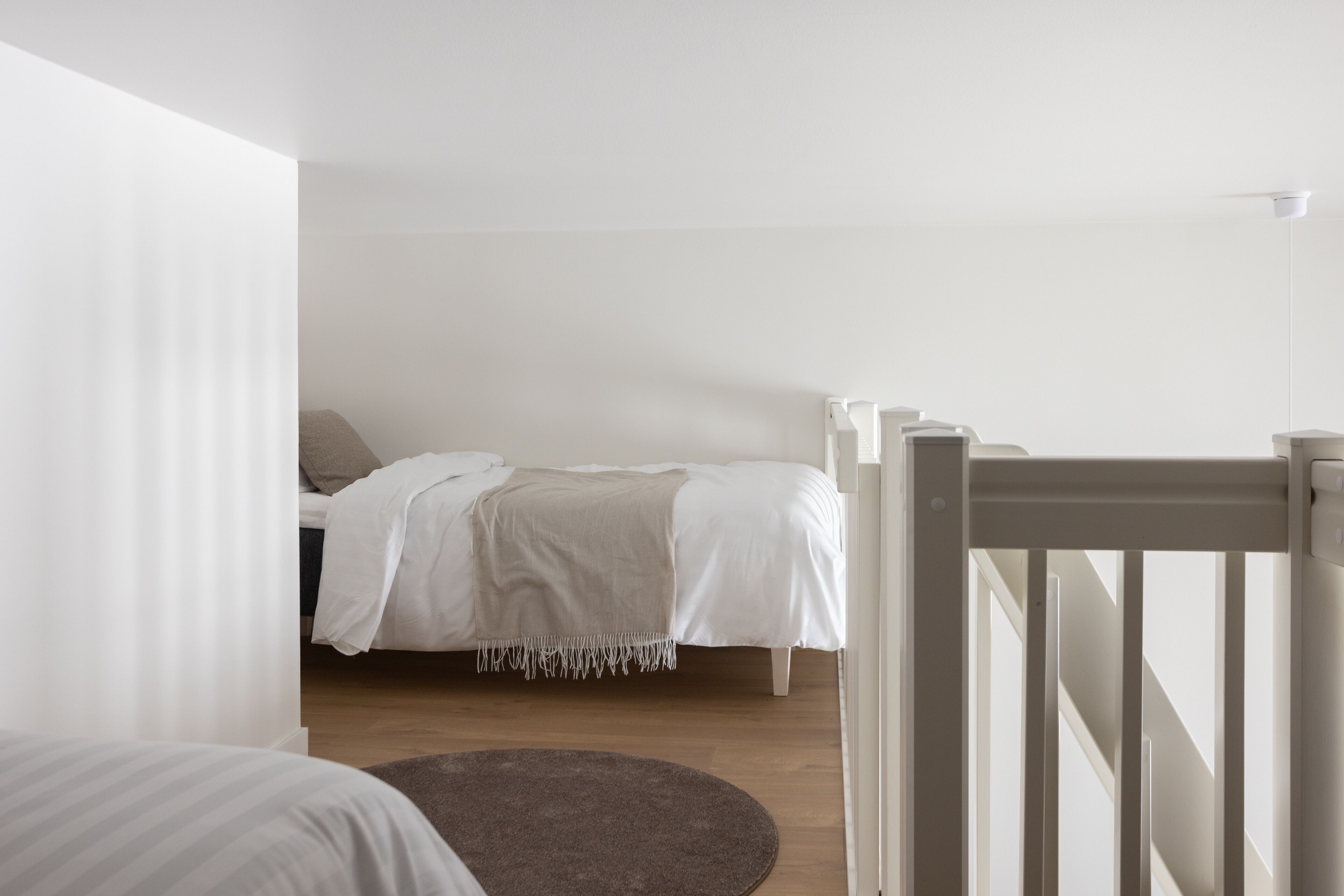 A bedroom with a bed, a round rug, and a white railing.