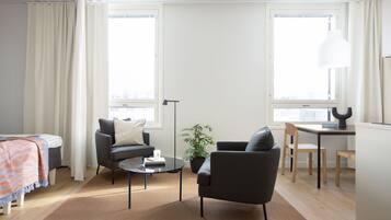 Ein modernes Wohnzimmer mit Sofa, Sesseln, einem Couchtisch und einem Essbereich mit Tisch und Stühlen. Eine Zimmerpflanze und eine Lampe sind ebenfalls vorhanden.