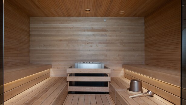 A sauna with wooden benches, a central heating unit, and a metal bucket. - Noli Malmi (Helsinki)