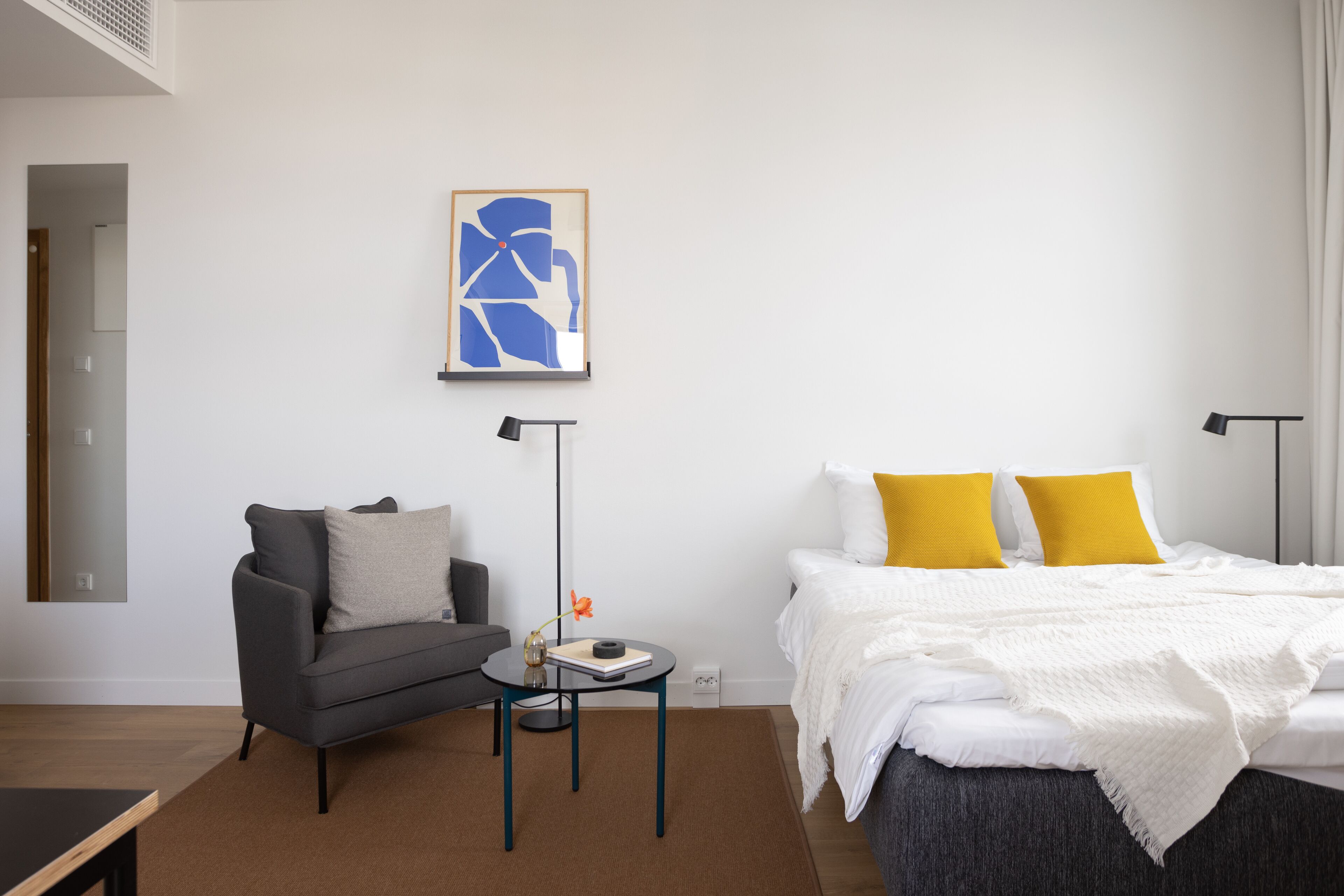 Una habitación de hotel moderna con una cama, un sofá, una mesita y una lámpara de pie.