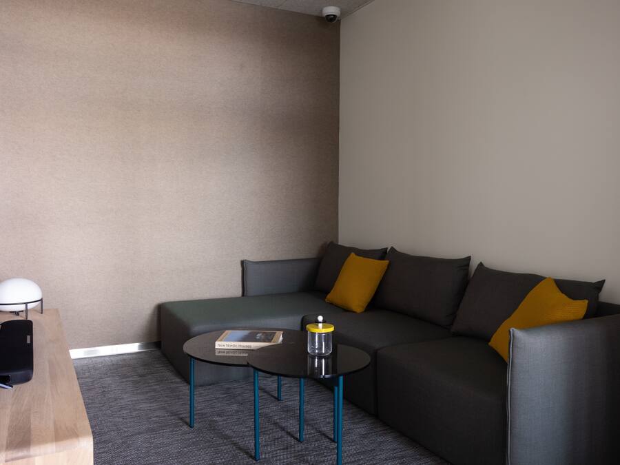 A modern hotel room with a grey sofa, a small round table, and a flat-screen TV on a wooden desk.