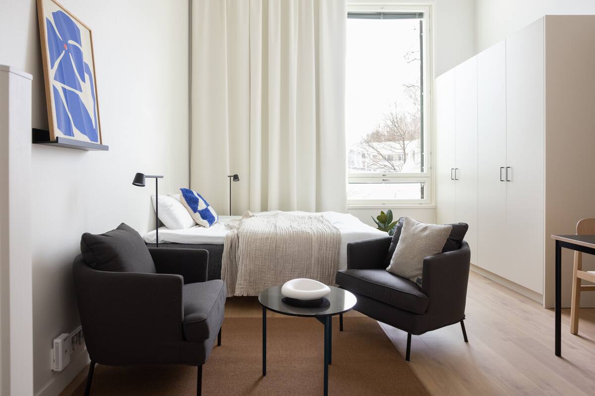 Um quarto moderno com uma cama, dois sofás, uma mesinha e uma janela com cortinas.