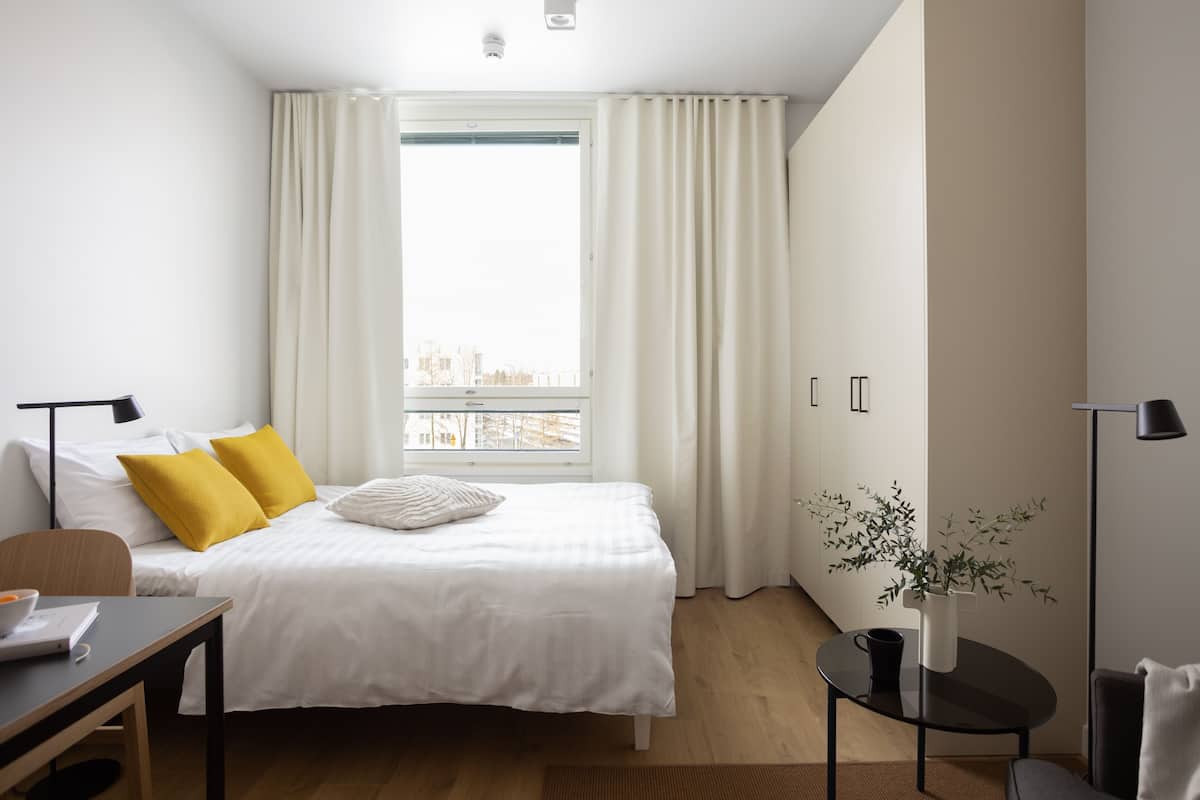 Quarto de hotel moderno com uma cama grande, uma escrivaninha e uma pequena mesa com uma planta.