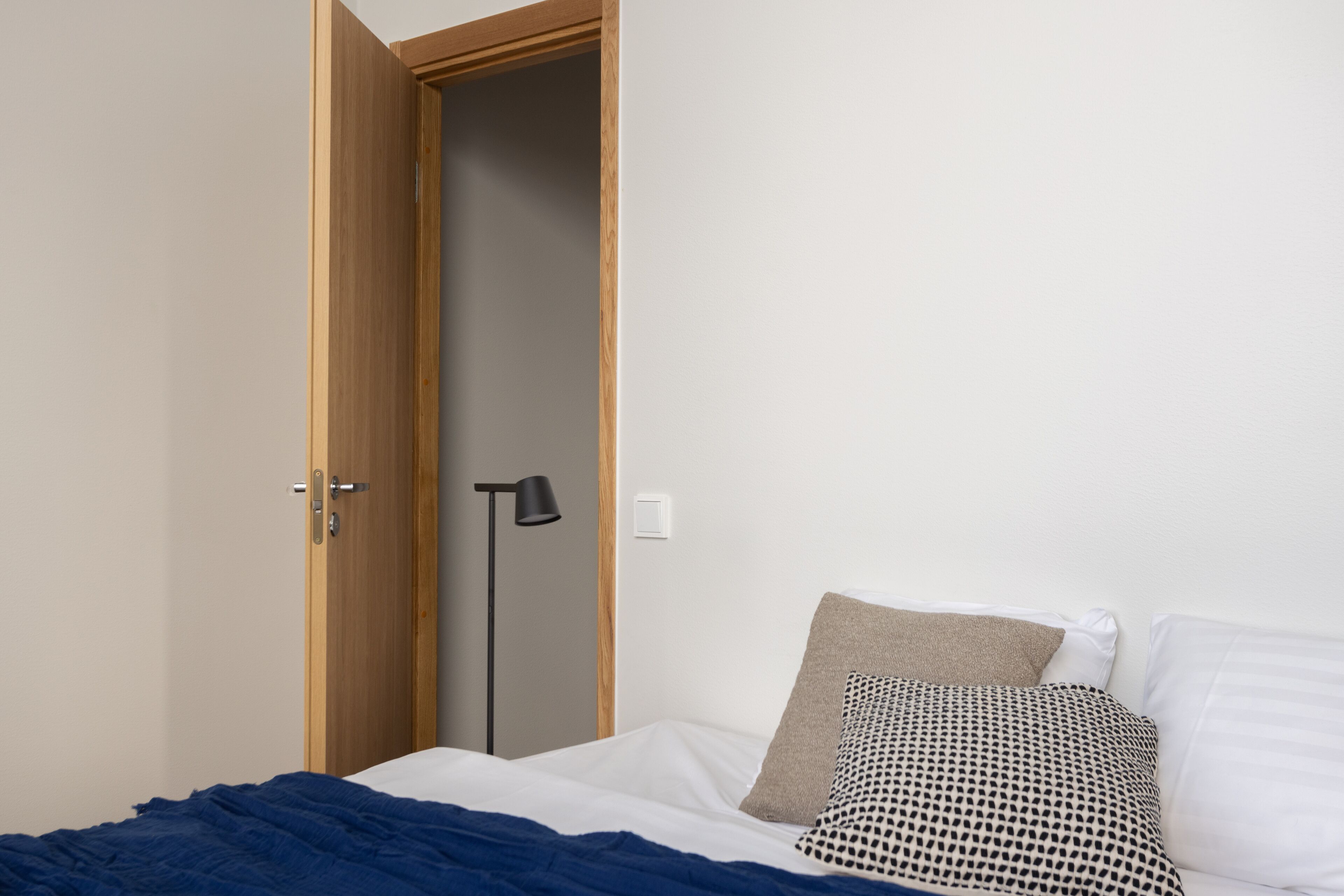 Quarto com cama, guarda-roupa de madeira, luminária de chão e tomada na parede.