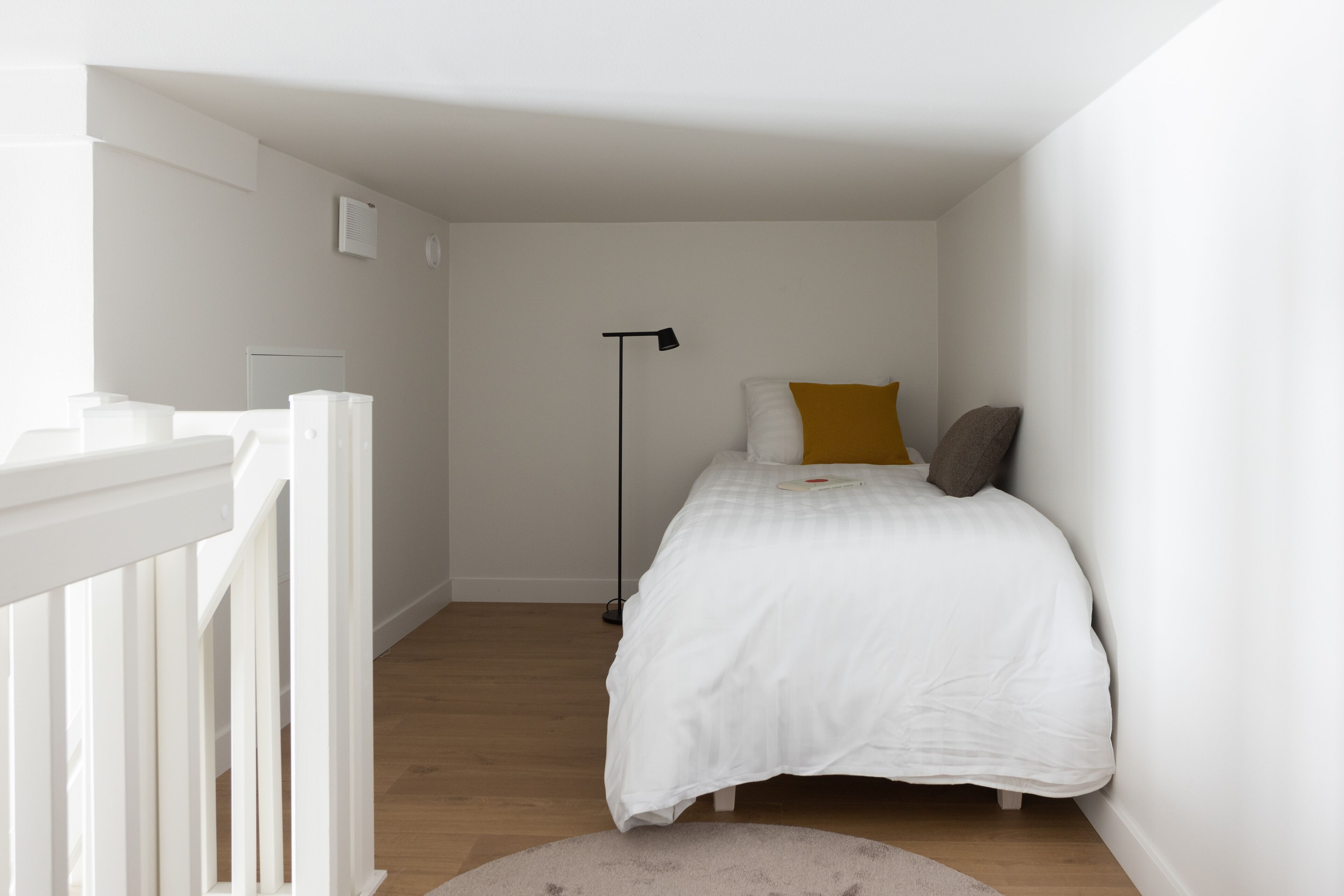 Une chambre avec un lit blanc, une lampe sur pied et une balustrade blanche.