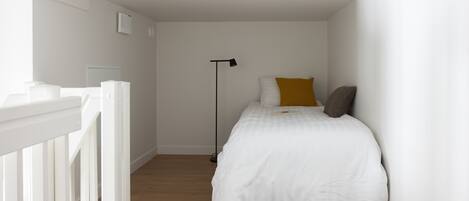 Une chambre avec un lit blanc, une lampe sur pied et une balustrade blanche.