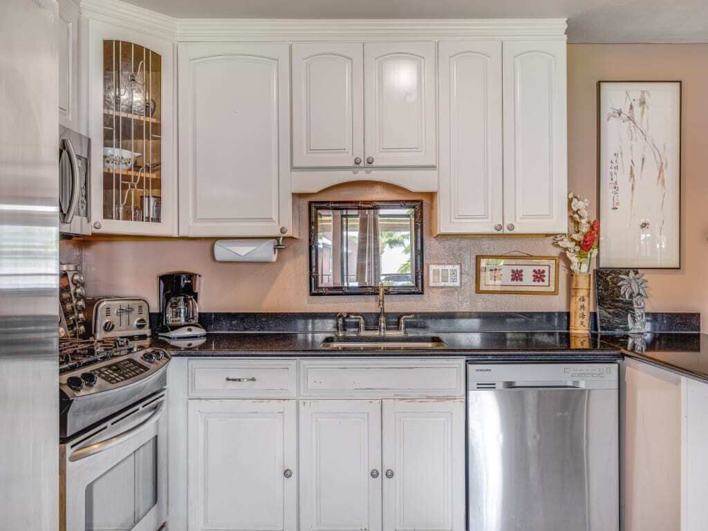 A kitchen with white cabinets, a stainless steel dishwasher, and a vintage stove.