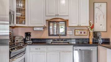 A kitchen with white cabinets, a stainless steel dishwasher, and a vintage stove.