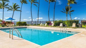 A swimming pool with a clear blue water, surrounded by palm trees and a fence.