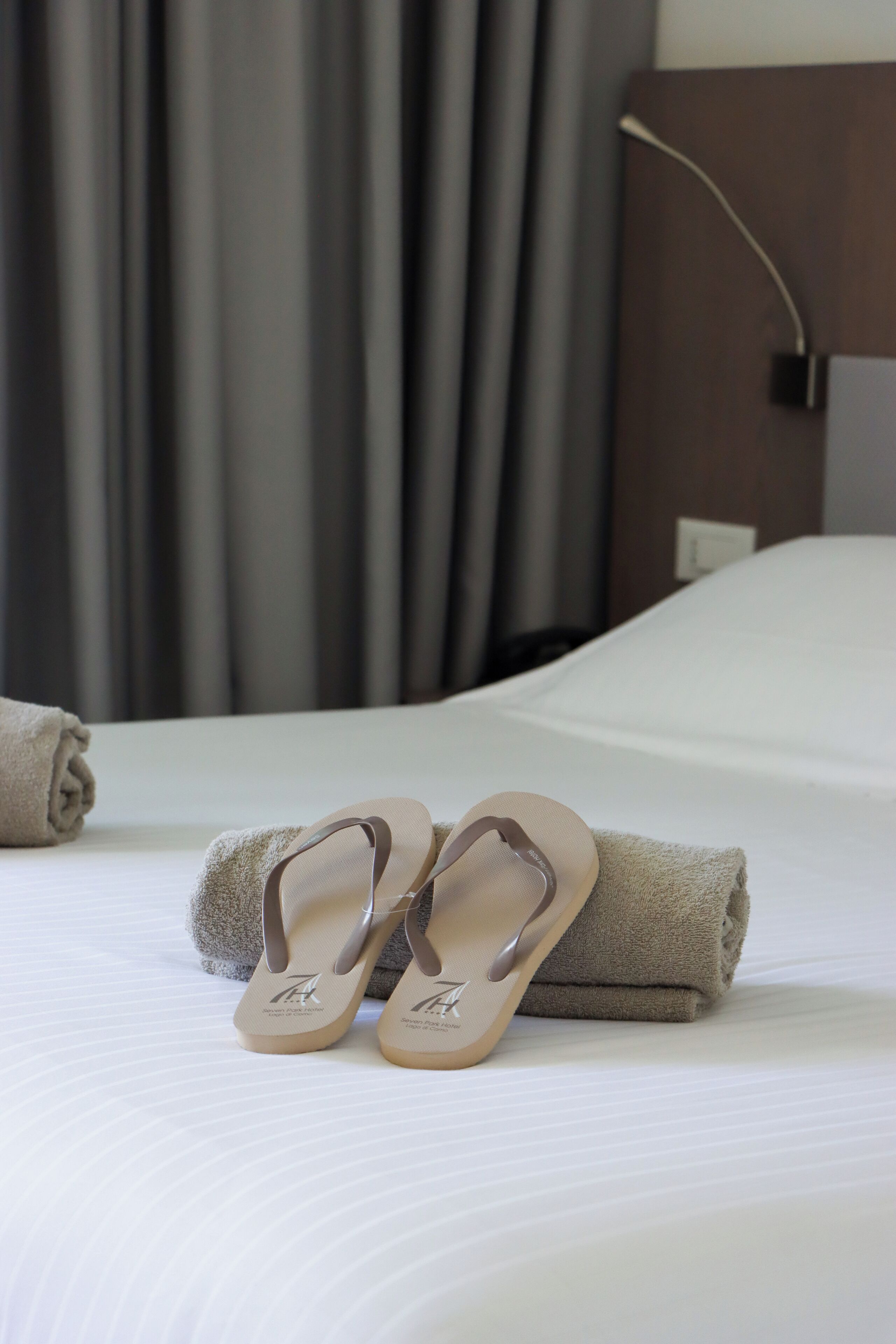 Una cama bien hecha con un par de chanclas beige y una toalla enrollada encima.