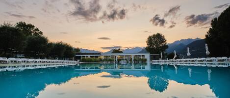 Un área de piscina tranquila con reflejos nítidos, rodeada de árboles y montañas al fondo.