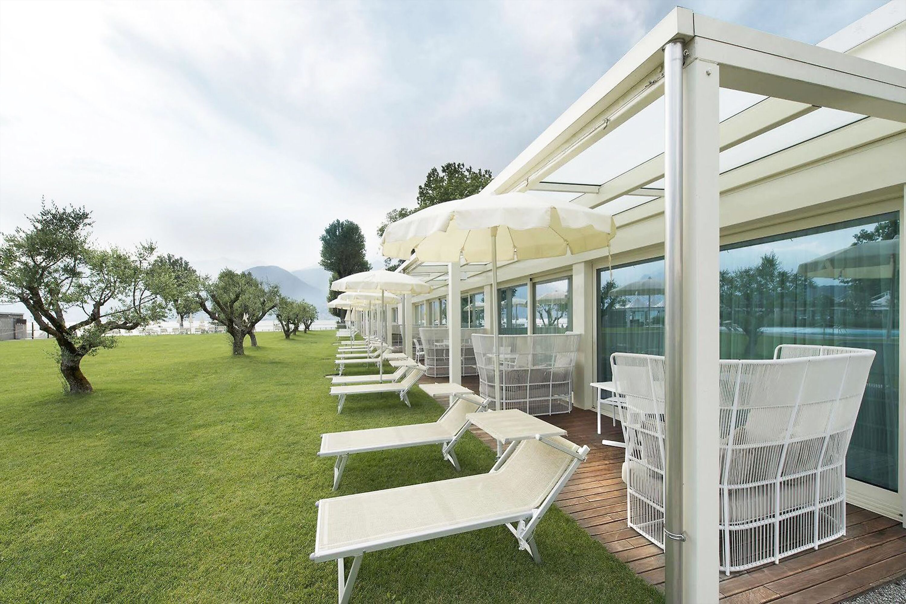 A covered outdoor seating area with white chairs and umbrellas, a wooden deck, and a view of the surrounding landscape.