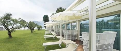 A covered outdoor seating area with white chairs and umbrellas, a wooden deck, and a view of the surrounding landscape.