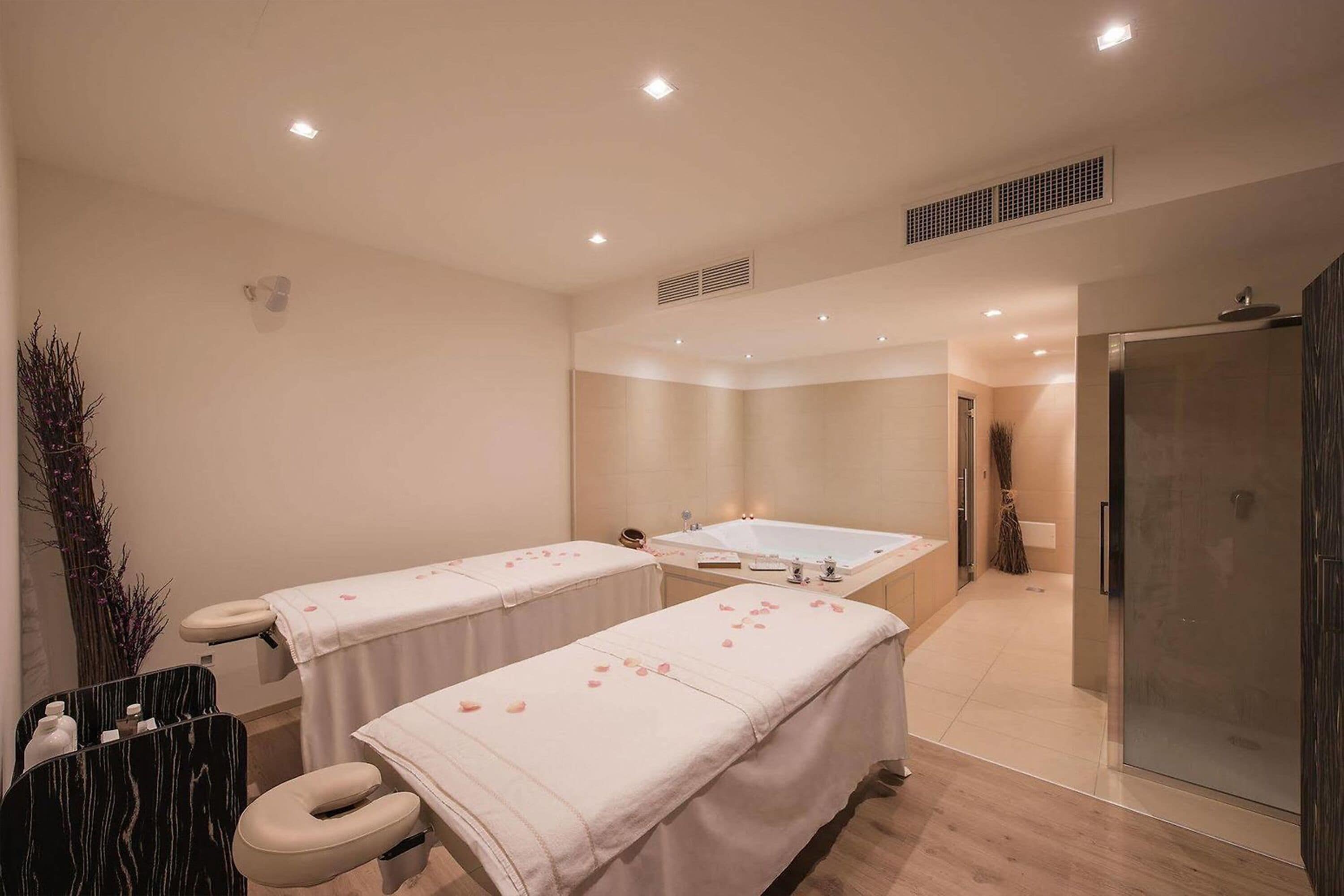 Un cuarto de spa con dos camillas de masaje, una tina grande y un box de ducha de vidrio.
