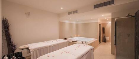 A spa room with two massage tables, a large bathtub, and a glass shower enclosure.