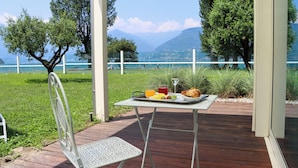 A dining table with a meal and a glass of juice on a deck with a view of a lake and mountains. - Seven Park Hotel Lake Como - Adults Only (Colico)