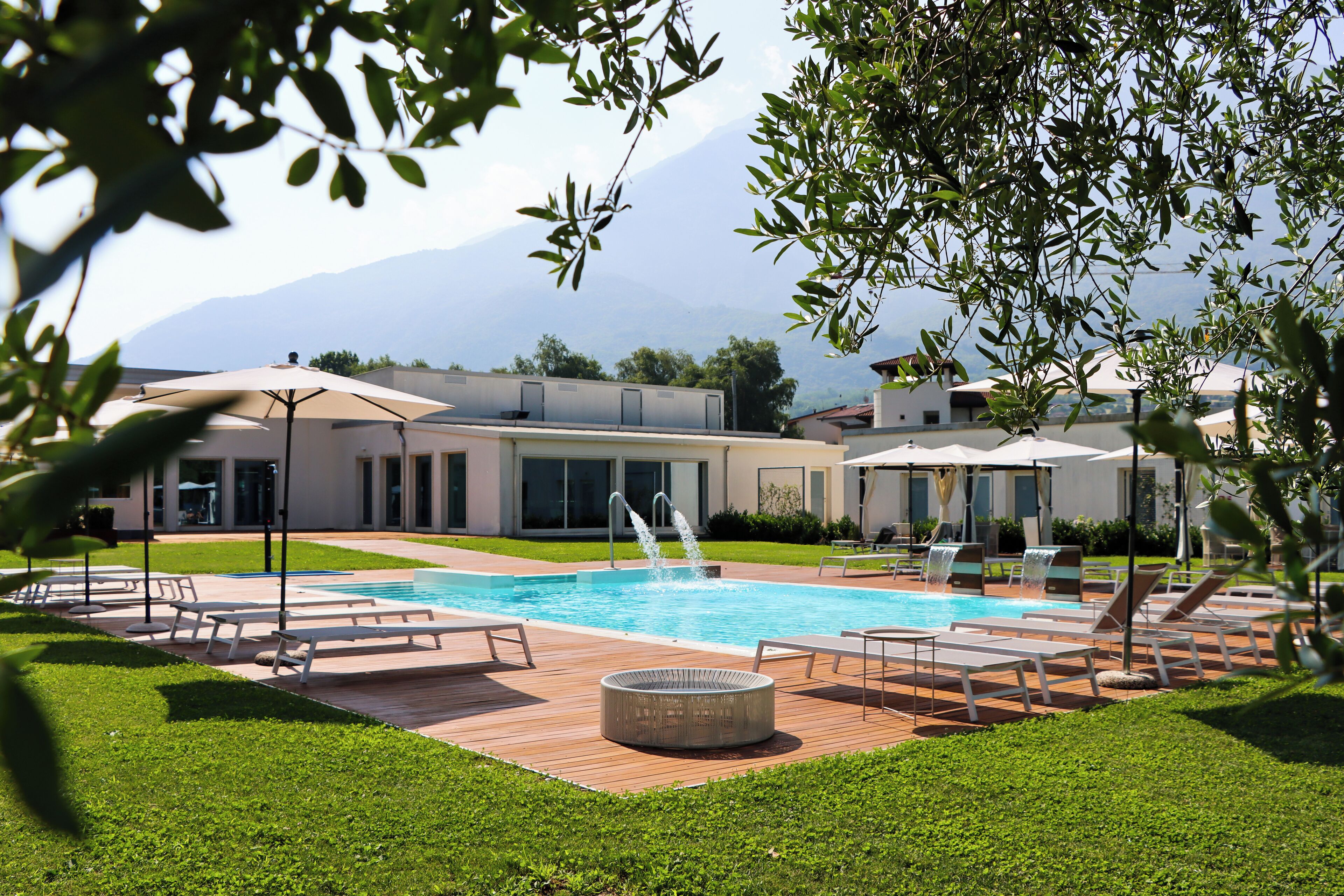 A pool area with lounge chairs, a hot tub, and a view of mountains.