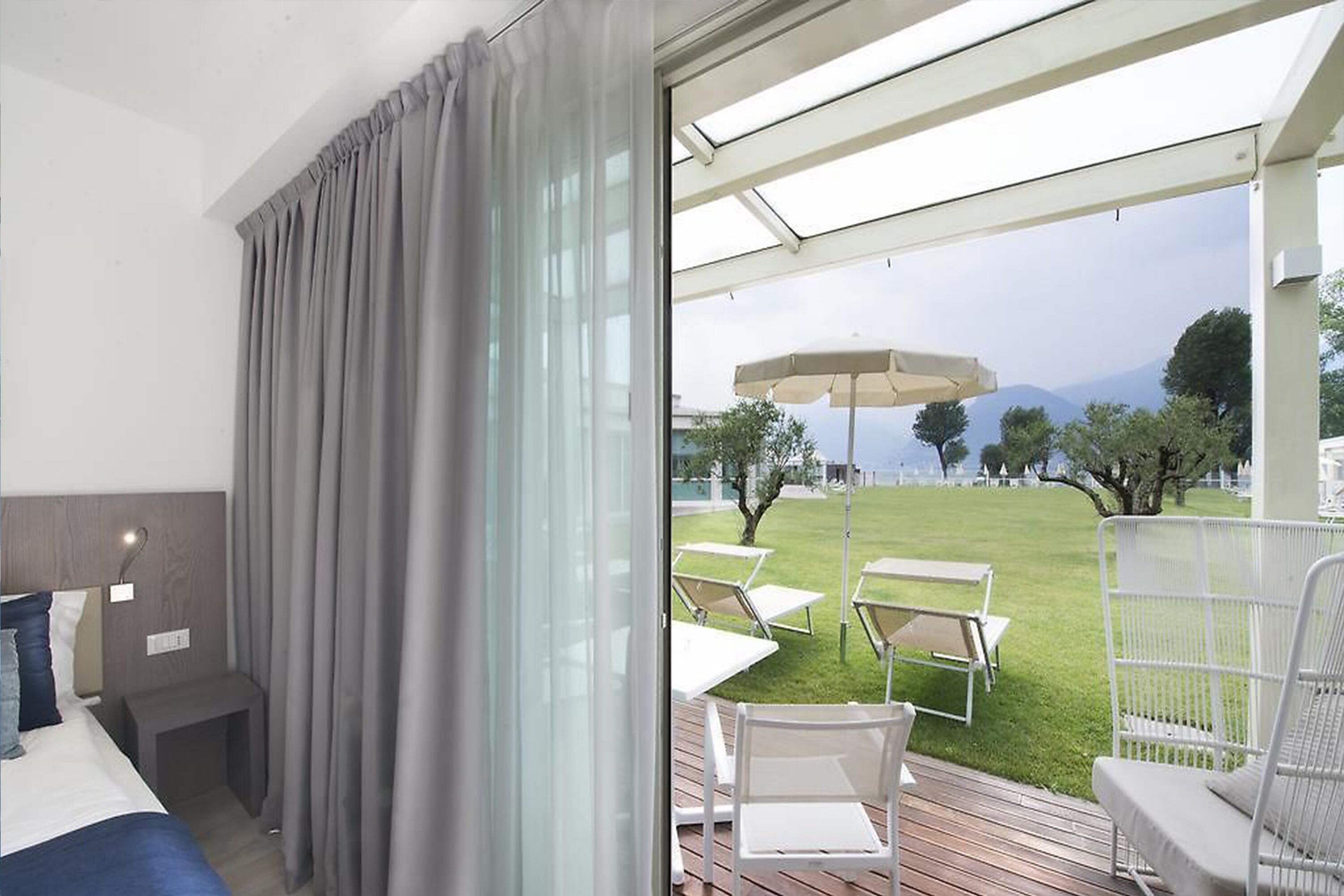 A hotel room with a bed, a bedside table, and a view of an outdoor patio with chairs and a table.
