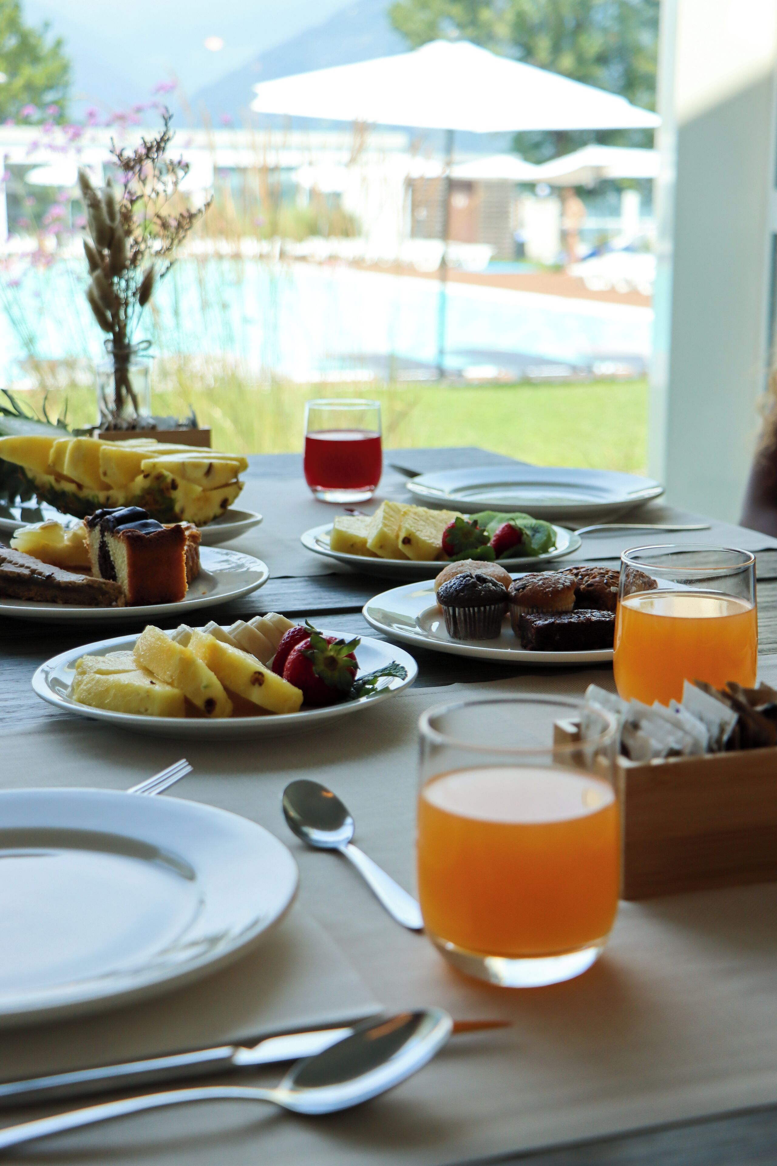 A table set for breakfast with various dishes, a glass of orange juice, and a view of the outdoors.