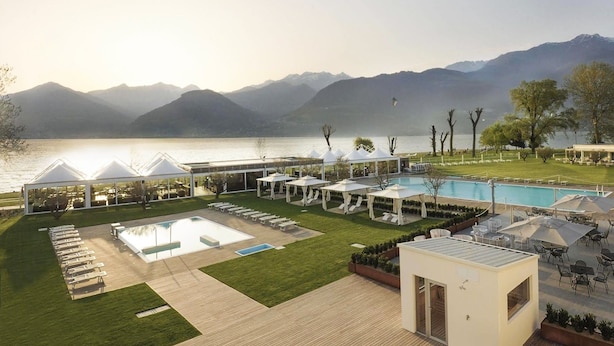 A resort with a pool, lounge chairs, and a view of mountains. - Seven Park Hotel Lake Como - Adults Only (Colico)