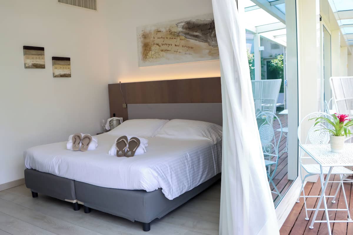 A neatly made bed with a headboard, a pair of slippers, and a wall art piece above it.