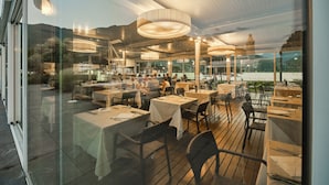 An outdoor dining area with tables and chairs, large windows, and a view of the mountains. - Seven Park Hotel Lake Como - Adults Only (Colico)