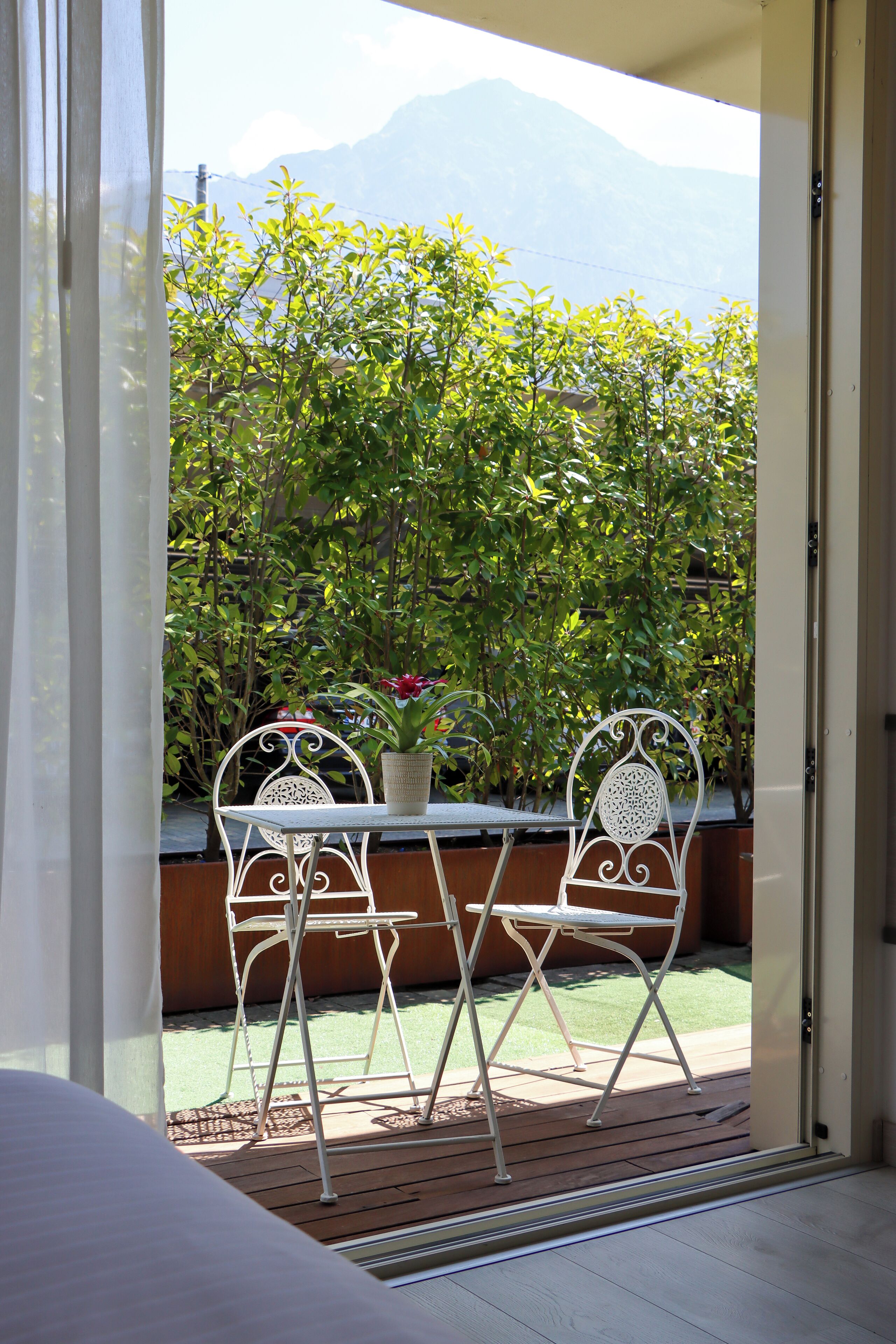 Un balcon avec une table et des chaises, une plante en pot, et une vue sur la verdure et les montagnes.
