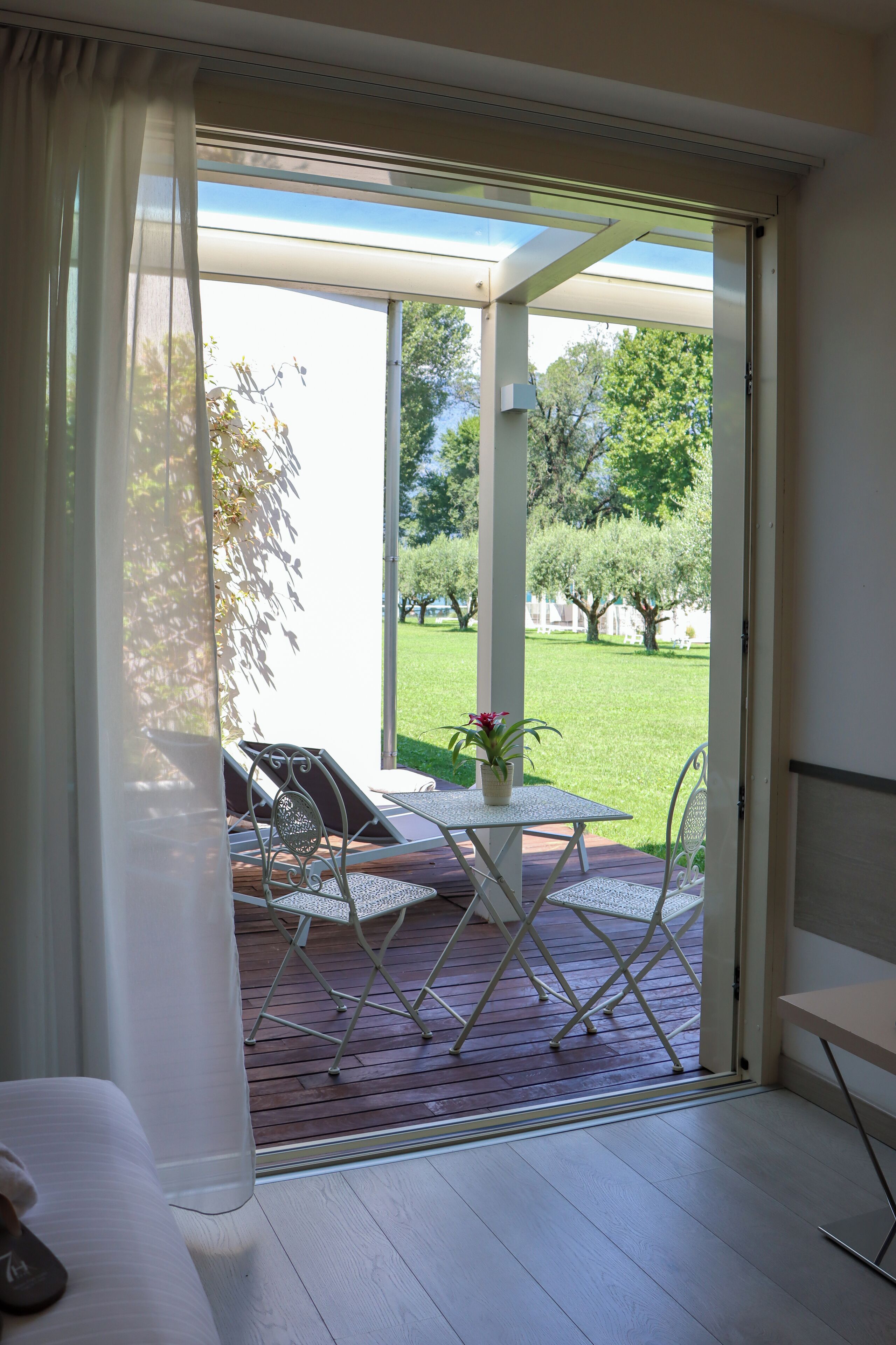 Una habitación con una puerta corrediza de vidrio que da a un patio exterior. El patio tiene una terraza de madera, una pequeña mesa con sillas y una planta en maceta.