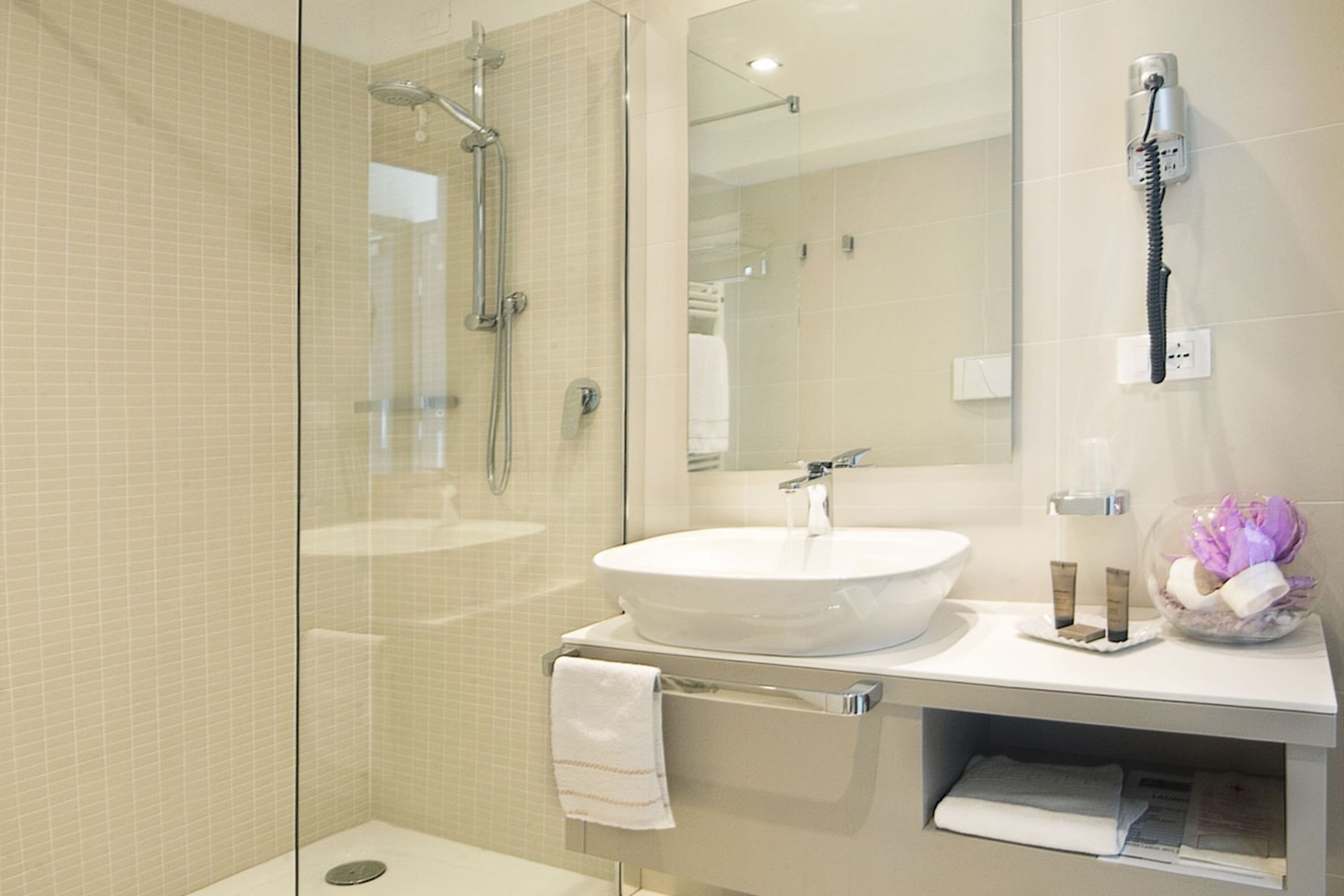 Un baño moderno con ducha envuelta en vidrio, un lavamanos blanco y un espejo sobre él.