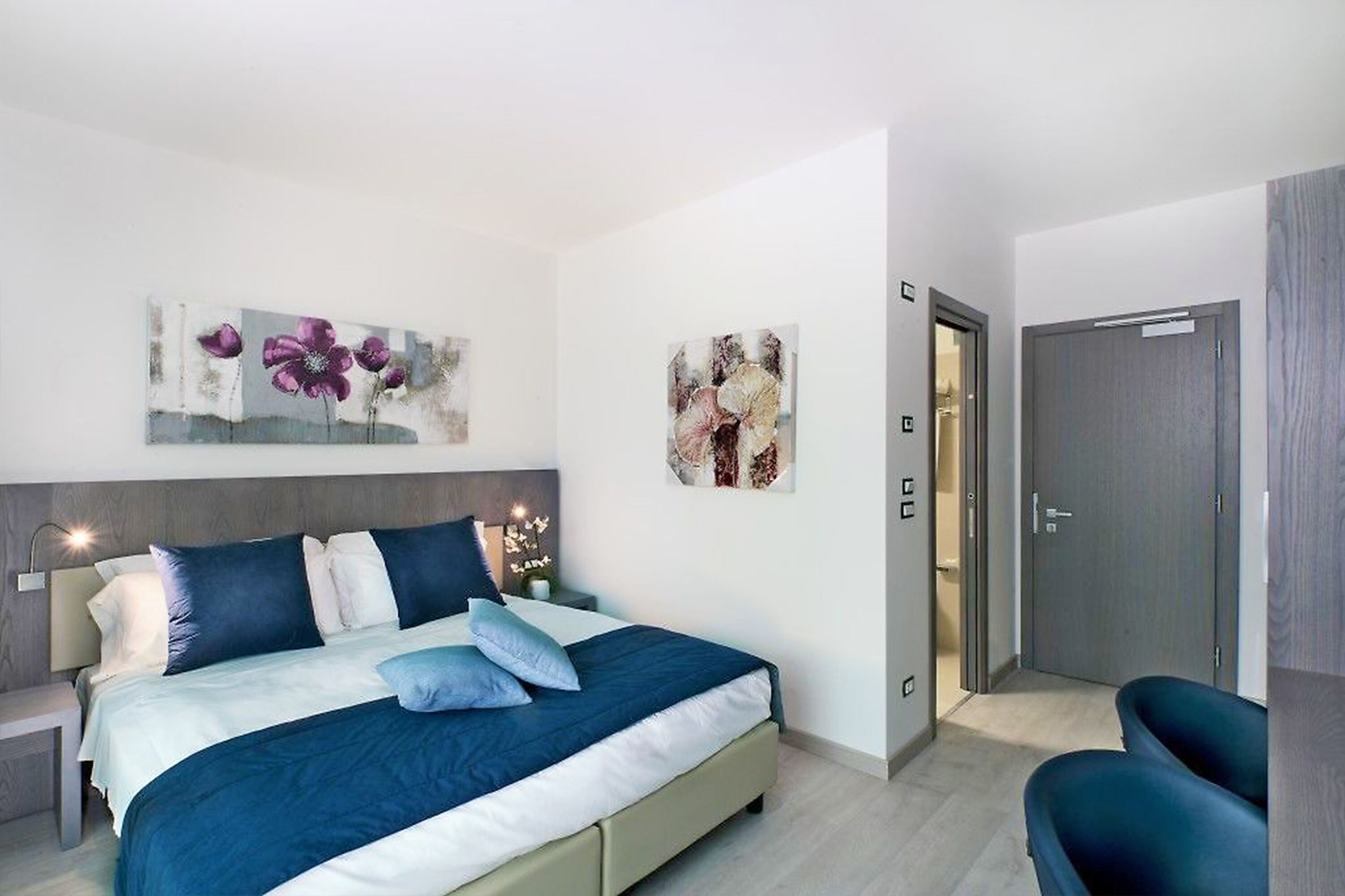 A modern bedroom with a bed, nightstands, and artwork on the walls.